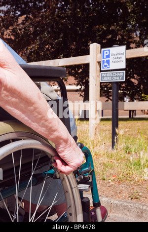 Scena quotidiana di anziani donna seduta su una sedia a rotelle in auto parcheggiate in blue badge parcheggio disabili bay e segno per gli utenti di sedia a rotelle solo Inghilterra REGNO UNITO Foto Stock