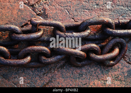 Links di Arrugginimento esteso la catena di ferro in appoggio sul red rock in riva al mare Foto Stock