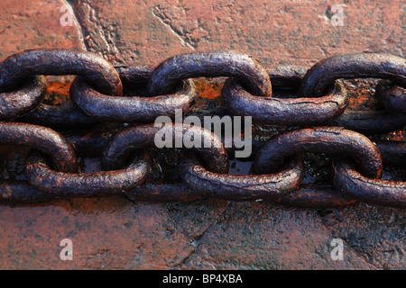 Links di Arrugginimento esteso la catena di ferro in appoggio sul red rock in riva al mare Foto Stock