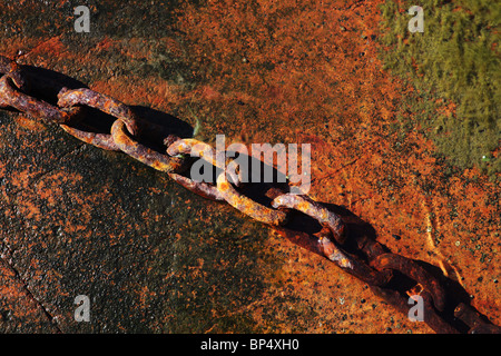 Links di Arrugginimento esteso la catena di ferro in appoggio sul red rock e in acqua al mare Foto Stock