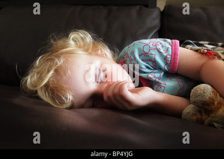 Bambino Toddler ragazza dorme tenendo un pisolino di pomeriggio su un divano succhiare il suo pollice modello rilasciato Foto Stock