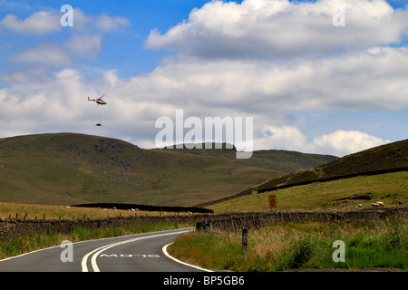 Elicottero che trasporta un'imbracatura con materiali da costruzione al di sopra del passaggio di serpente, Derbyshire. Foto Stock