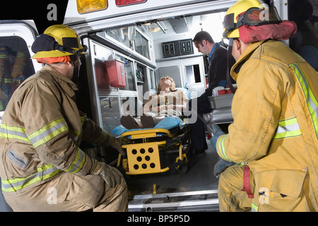 Vigili del fuoco guardando alla vittima in ambulanza Foto Stock