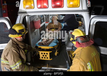 Vigili del fuoco guardando alla vittima in ambulanza Foto Stock