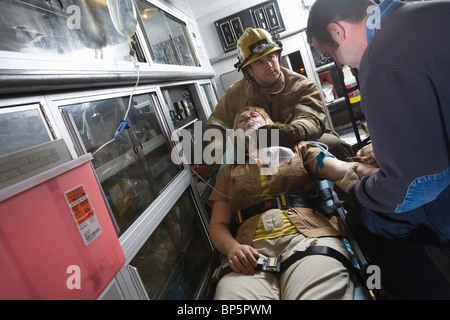 Vigile del fuoco e il personale paramedico ad aiutare la donna in ambulanza Foto Stock