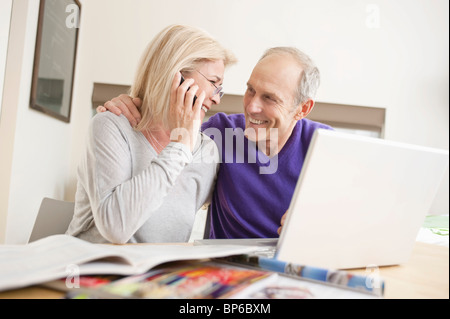 Donna che parla su un telefono cellulare seduto con suo marito davanti a un computer portatile Foto Stock