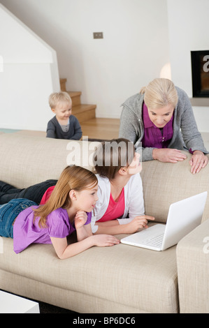 Due ragazze usando un computer portatile su un lettino con la loro nonna Foto Stock