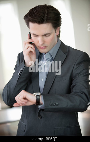 Imprenditore controllando il tempo e a parlare su un telefono mobile Foto Stock