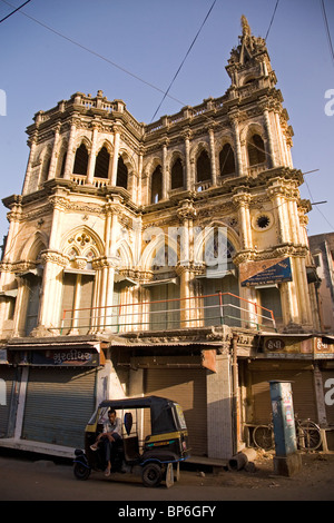 Un rickshaw conducente siede di fronte a una volta che-grande edificio in Junagadh, Gujarat, India. Foto Stock