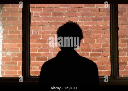 Silhouette di un uomo che guarda fuori della finestra in corrispondenza di un muro di mattoni Foto Stock
