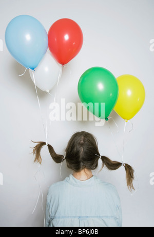 Vista posteriore di una ragazza con palloni di elio legato al suo pigtail Foto Stock
