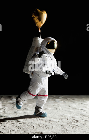 Un astronauta sulla luna tenendo un cuore a forma di palloncino elio Foto Stock