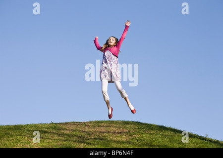 Una ragazza saltando su una collina erbosa Foto Stock