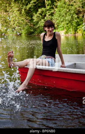 Una giovane donna in una barca a remi gli spruzzi di acqua con il suo piede Foto Stock