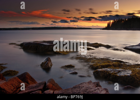 Un bellissimo tramonto Maine con arancione, rosa e azzurro del cielo. Le rocce di granito rosa in primo piano dal bagliore del sole al tramonto. Foto Stock