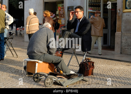 Città scena di un uomo vecchio shining le scarpe di un imprenditore a Lisbona, Portogallo. Foto Stock