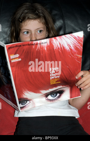 Ragazza giovane la lettura di una storia circa la American pop star Katy Perry in The Guardian weekend magazine Foto Stock