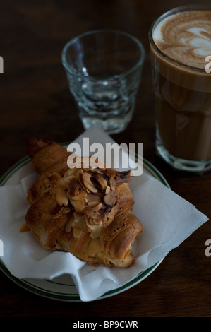 Un croissant alle mandorle e caffè latte servita su una tavola di legno in una caffetteria alla moda in Toronto. Foto Stock