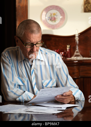 Uomo anziano seduto alla scrivania guardando attraverso le bollette Foto Stock