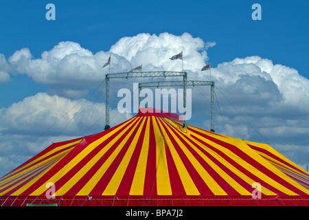 Striped tenda del circo contro un cielo blu con nuvole soffici. Posizione orizzontale Foto Stock