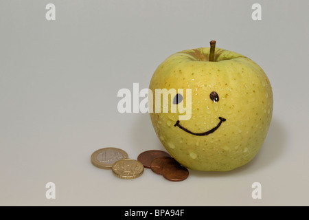 Smiley di mela gialla con gocce di acqua e di monete metalliche in euro Foto Stock