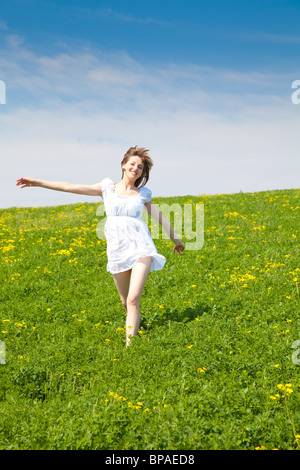 Giovane donna in esecuzione attraverso un campo di erba in primavera con colorate sciarpe Foto Stock