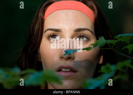 Venti anni di donna guarda fuori da dietro le foglie nei boschi. Foto Stock