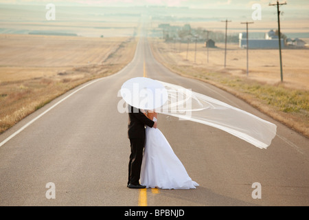 Tre colline, Alberta, Canada; la sposa e lo sposo in un abbraccio in piedi su una strada rurale in Alberta Foto Stock