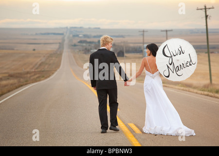 Tre colline, Alberta, Canada; la sposa e lo sposo su una strada con la sposa tenendo un ombrellone con le parole 'appena sposato' su di esso Foto Stock