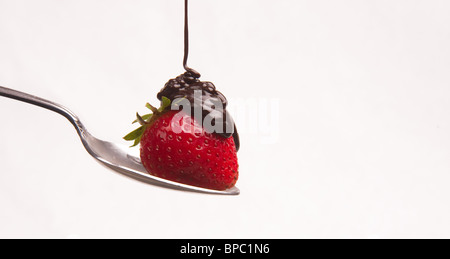 Sciroppo al cioccolato gocce su una fragola seduto su un cucchiaio isolato su bianco Foto Stock