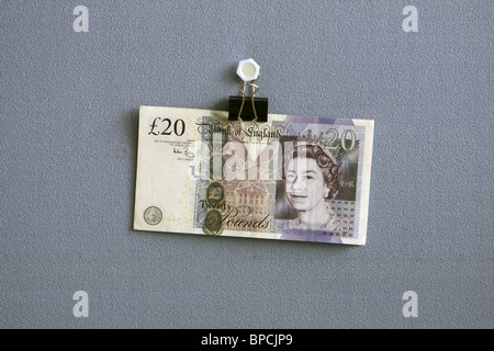 £20 nota appeso un bulldog clip contro un panno blu sullo sfondo Foto Stock