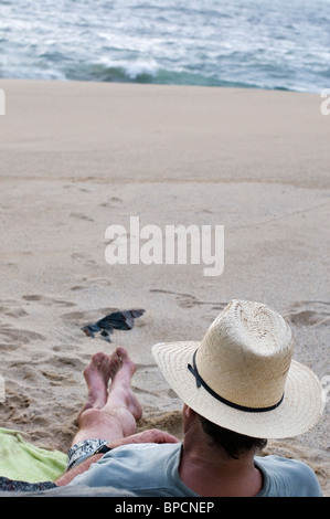 Vista da dietro di un uomo che indossa abiti casual e un cappello di paglia relax su una sabbiosa spiaggia poco affollate in Messico. Foto Stock