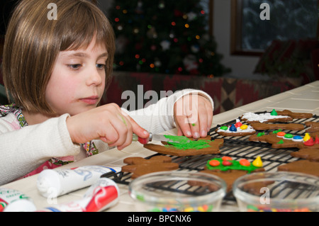 Un simpatico bambina decora gingerbread cookie. Foto Stock