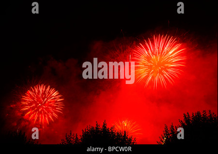 Fuochi d' artificio irrompe nel cielo di notte contro uno sfondo di rosso il fumo. Spazio per il testo nel buio del cielo notturno. Foto Stock