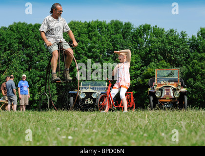 Una ragazza giovane su una piccola bicicletta guarda un uomo ciclo passato su un penny farthing. Foto Stock