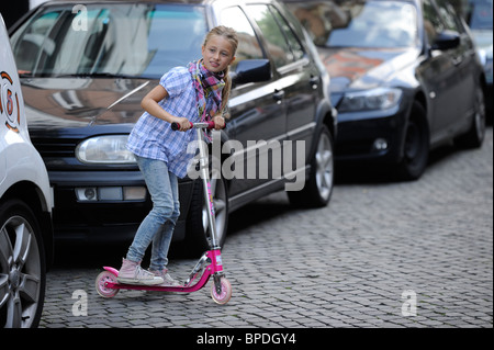 Bambina di otto anni con lo scooter in una strada residenziale a Duesseldorf in Germania. Foto Stock