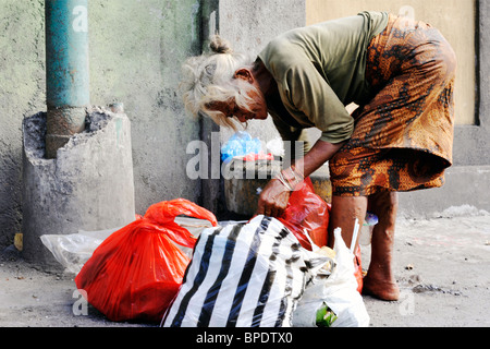 Anziani donna locale di scavenging del cibo nel cestino della spazzatura in una strada di Kuta Bali Foto Stock