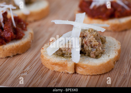 Verde Verde Oliva tapenade su leggermente tostate fette di baguette e rabboccato con fresco parmigiano grattugiato. Foto Stock