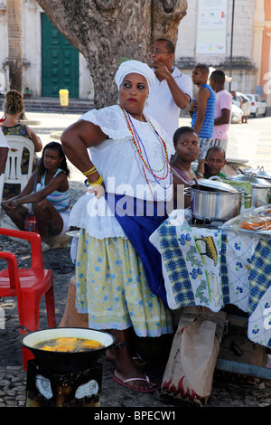 Bahiana donna nel tradizionale abito bianco (Baiana) la vendita di cibo di strada presso il quartiere Pelourinho, Salvador, Bahia, Brasile. Foto Stock