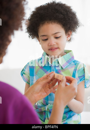 Madre mettendo cerotto sul dito della figlia Foto Stock