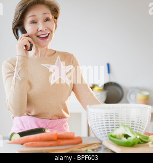 Donna giapponese utilizzando il telefono in cucina Foto Stock