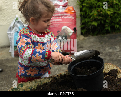 Un bambino di sei anni ragazza caucasica riempire una pentola con il compost pronto per piantare in giardino Foto Stock