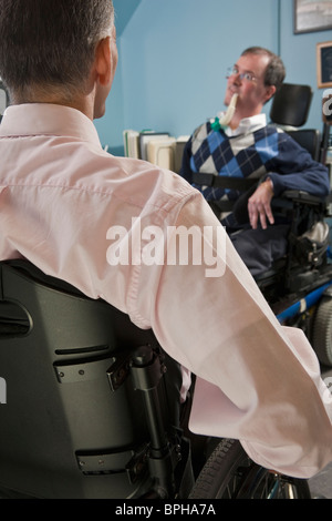 Due imprenditori in un ufficio, uno con la distrofia muscolare e la respirazione ventilatore e un altro con lesioni del midollo spinale Foto Stock