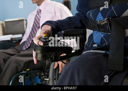 Imprenditore con distrofia muscolare di Duchenne utilizzando una sedia a rotelle motorizzata accanto alla sua collega con lesioni del midollo spinale Foto Stock