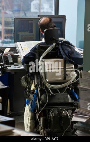 Imprenditore con distrofia muscolare di Duchenne in una sedia a rotelle motorizzata lavora in un ufficio Foto Stock