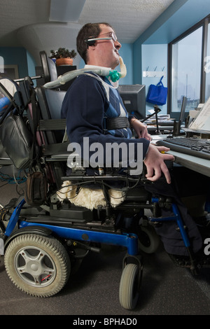 Imprenditore con distrofia muscolare di Duchenne in una sedia a rotelle motorizzata lavora in un ufficio Foto Stock