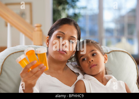 Ispanico donna seduta con la figlia e la holding flaconi portapillole Foto Stock