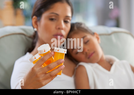 Ispanico donna seduta con la figlia e la holding flaconi portapillole Foto Stock