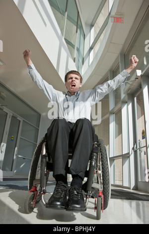 Imprenditore con lesioni al midollo spinale in una sedia a rotelle con le braccia sollevate Foto Stock