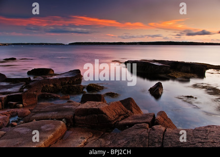 Un bellissimo tramonto Maine con arancione, rosa e azzurro del cielo. Le rocce di granito rosa in primo piano dal bagliore del sole al tramonto. Foto Stock